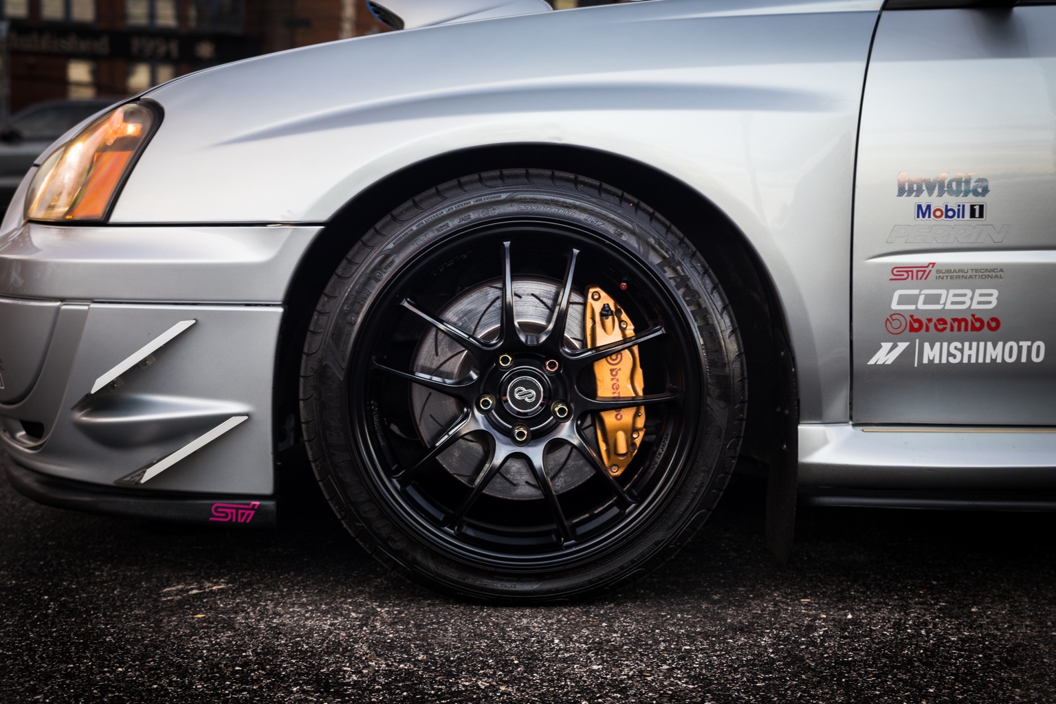 Close-up of a black performance wheel and gold Brembo brake caliper on a silver Subaru STI