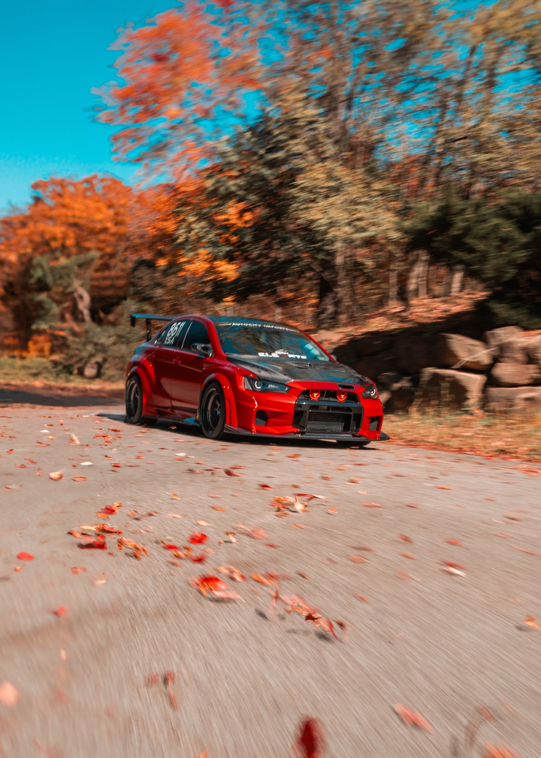 Red Mitsubishi Lancer Evolution moving through autumn scenery