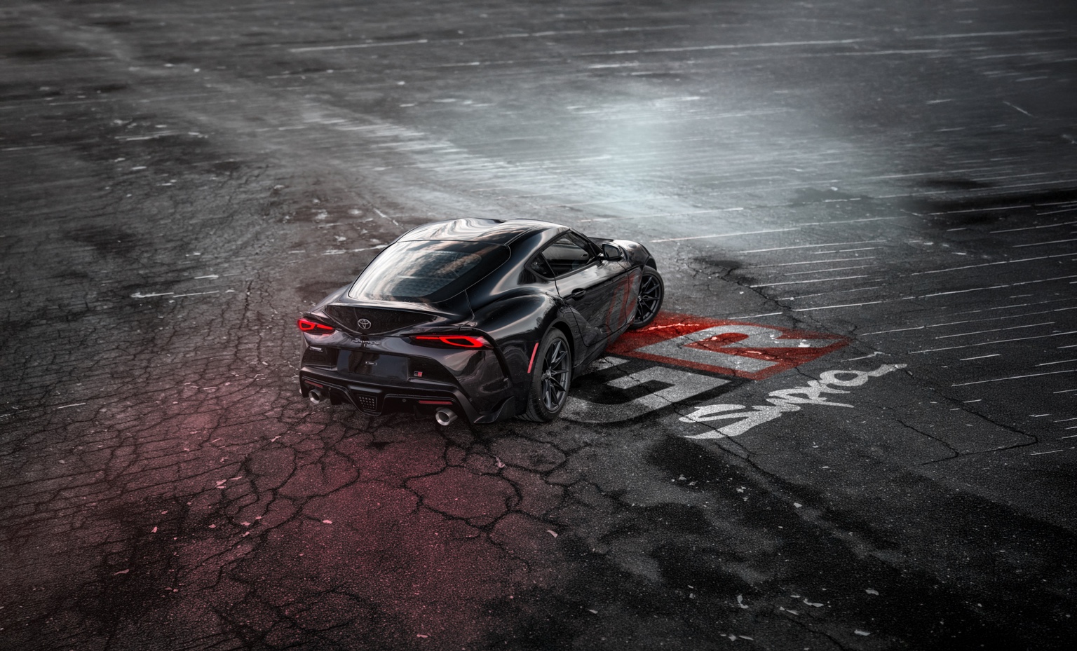 Black Toyota GR Supra in a dark parking lot with red light trails