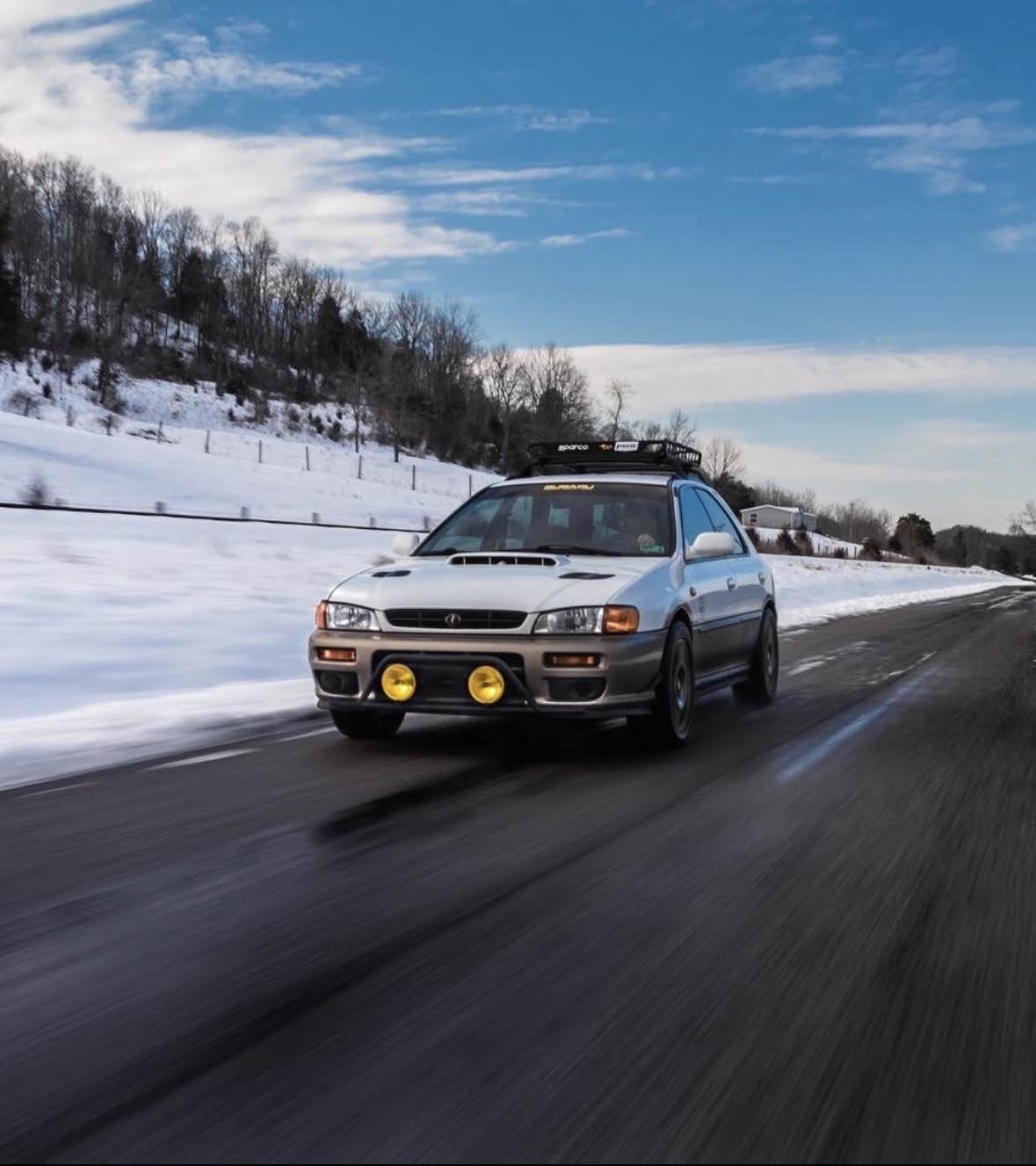 Silver Subaru driving along a snow-lined road